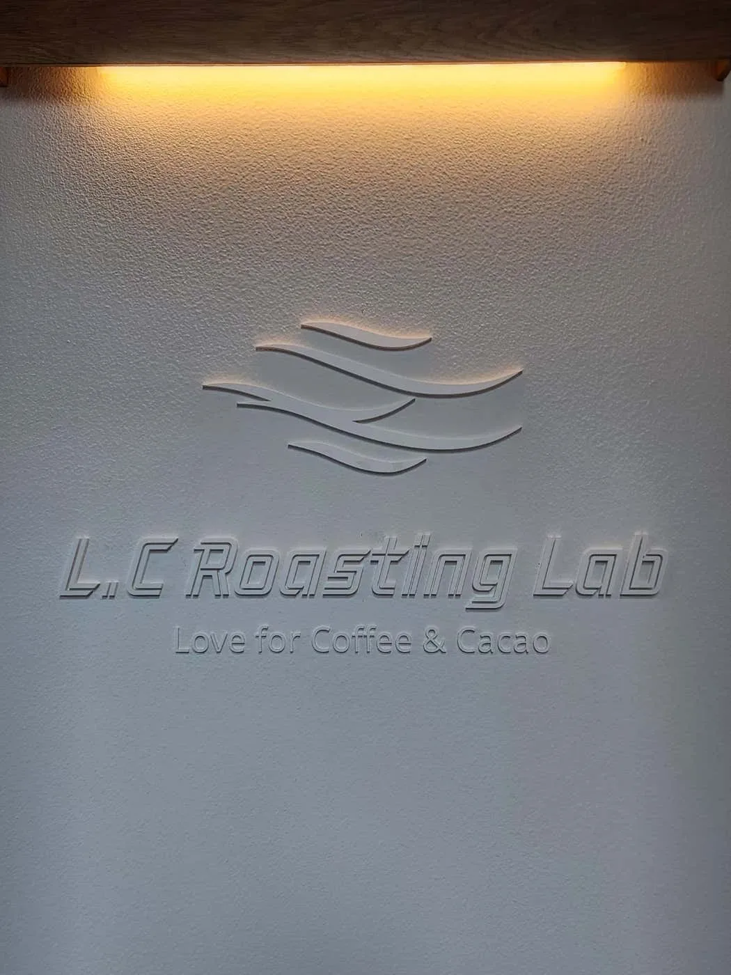 흰 벽에 양각으로 새긴 L.C Roasting Lab 로고 아래에 Love for Coffee & Cacao라는 문구가 적혀 있습니다.